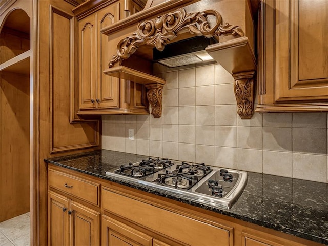 kitchen featuring stainless steel gas stovetop, custom range hood, dark stone counters, and tasteful backsplash