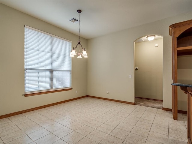 tiled empty room with plenty of natural light and a chandelier