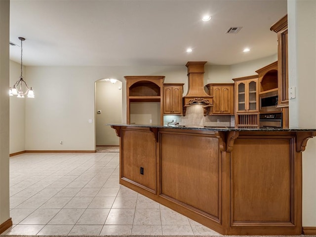 kitchen with premium range hood, oven, tasteful backsplash, a breakfast bar area, and a chandelier