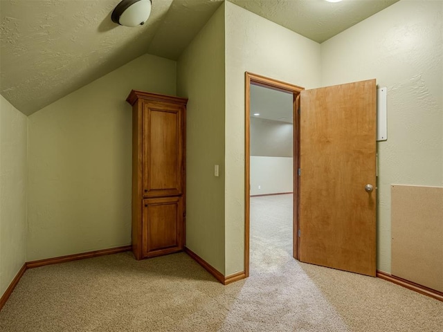 additional living space with a textured ceiling, light colored carpet, and lofted ceiling