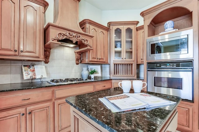 kitchen featuring appliances with stainless steel finishes, a center island, dark stone countertops, custom range hood, and decorative backsplash