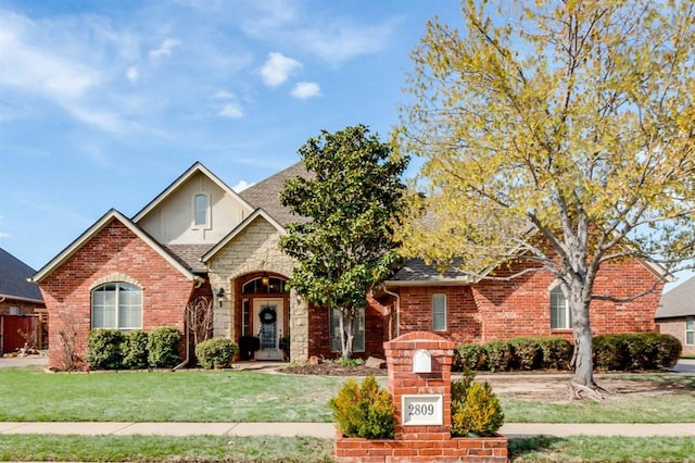 view of front facade featuring a front yard, brick siding, and roof with shingles