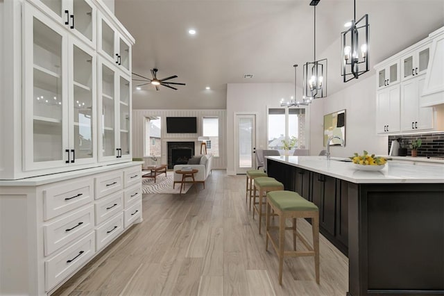 kitchen with tasteful backsplash, white cabinets, an island with sink, and ceiling fan with notable chandelier