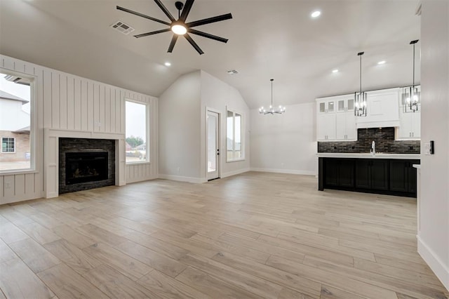 unfurnished living room with a stone fireplace, light hardwood / wood-style floors, sink, vaulted ceiling, and ceiling fan