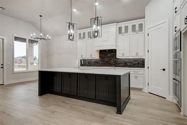 kitchen with lofted ceiling, custom exhaust hood, sink, an island with sink, and white cabinets