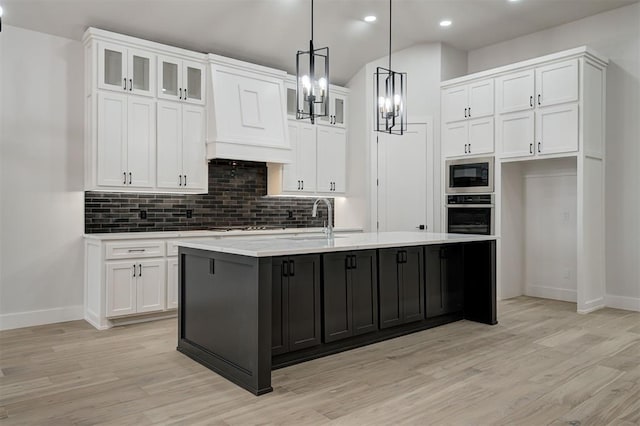 kitchen featuring decorative light fixtures, white cabinets, a center island with sink, and appliances with stainless steel finishes