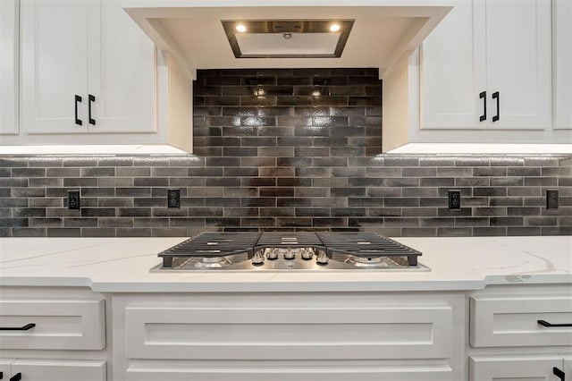 kitchen with stainless steel gas stovetop, decorative backsplash, white cabinets, and light stone countertops