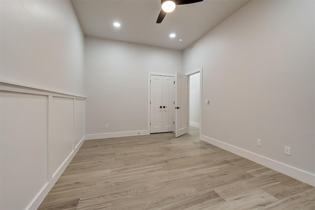 unfurnished room with ceiling fan, light wood-type flooring, and a high ceiling