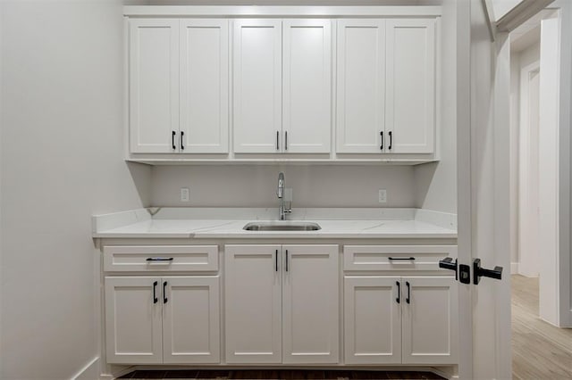 interior space with light wood-type flooring, white cabinetry, light stone counters, and sink