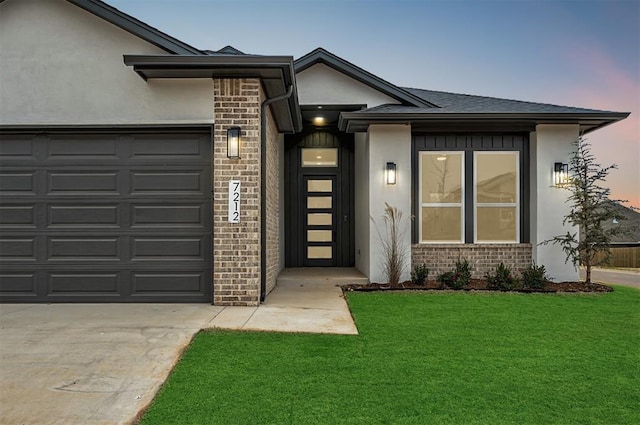 exterior entry at dusk featuring a garage and a lawn