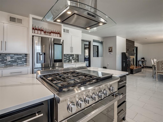 kitchen with decorative backsplash, light stone countertops, appliances with stainless steel finishes, white cabinets, and island range hood