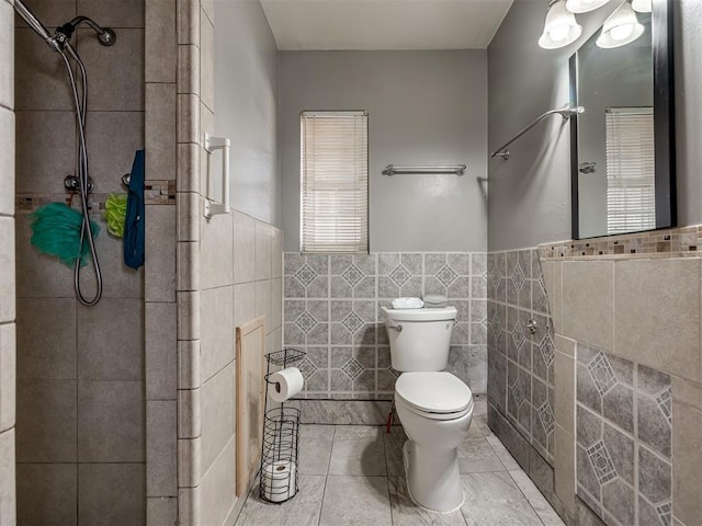 bathroom with toilet, tile patterned flooring, tile walls, and tiled shower