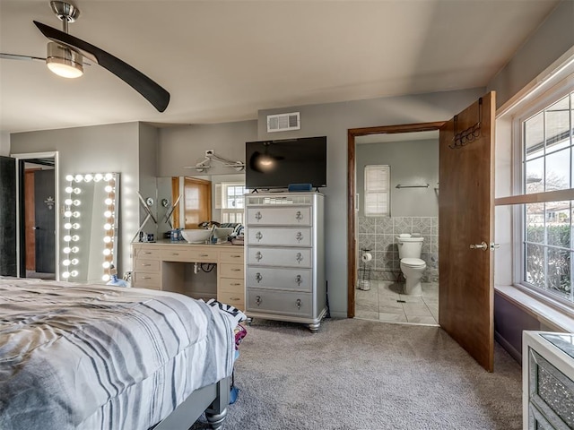 bedroom with ceiling fan, light colored carpet, tile walls, and ensuite bath