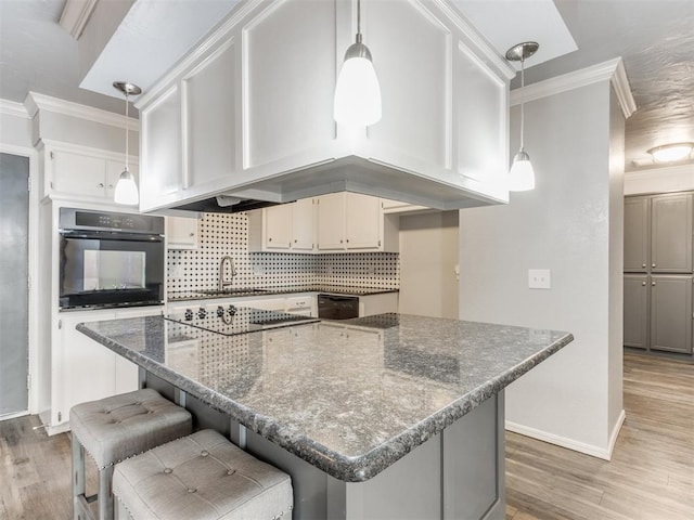 kitchen with a center island, dark stone counters, black appliances, ornamental molding, and wood-type flooring