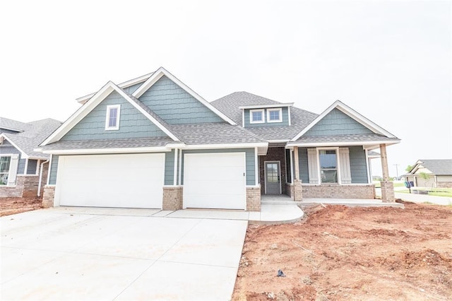 craftsman house with covered porch, roof with shingles, brick siding, driveway, and a garage