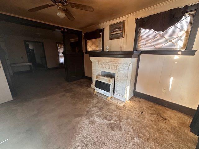 unfurnished living room with heating unit, crown molding, carpet floors, and ceiling fan