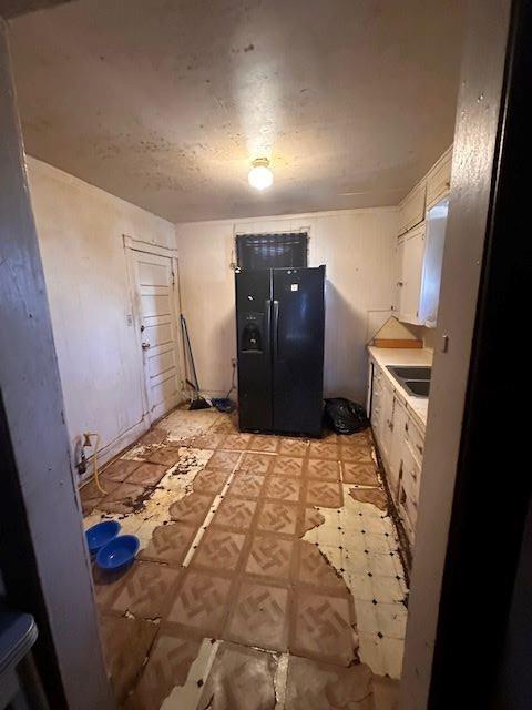 kitchen featuring white cabinets, black refrigerator with ice dispenser, and sink