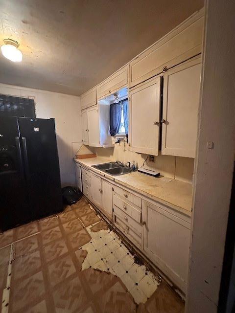 kitchen featuring white cabinets, black fridge, and sink