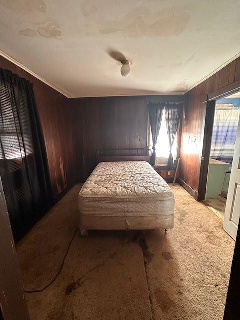 carpeted bedroom featuring wood walls and ornamental molding