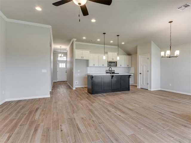 kitchen featuring a center island with sink, white cabinets, decorative light fixtures, and light hardwood / wood-style flooring