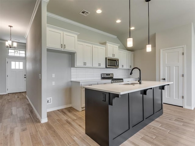 kitchen featuring white cabinets, stainless steel appliances, hanging light fixtures, and an island with sink