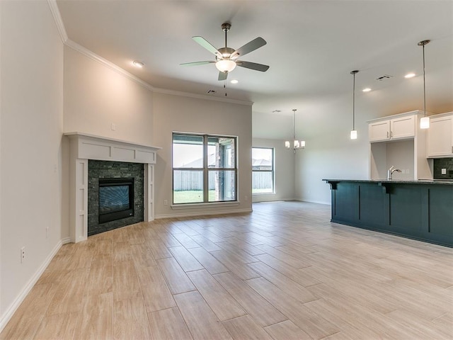 unfurnished living room featuring ceiling fan with notable chandelier, sink, crown molding, a fireplace, and light hardwood / wood-style floors