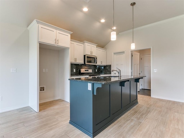 kitchen with dark stone counters, stainless steel appliances, white cabinets, hanging light fixtures, and an island with sink