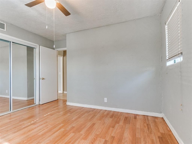 unfurnished bedroom featuring ceiling fan, a closet, a textured ceiling, and light hardwood / wood-style flooring