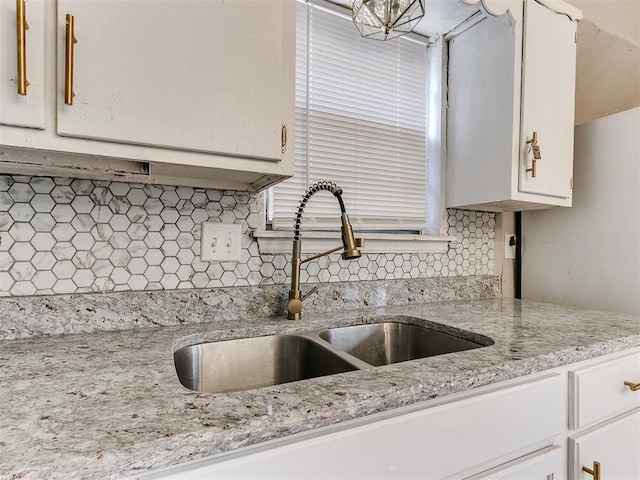 kitchen featuring backsplash, white cabinetry, sink, and light stone counters