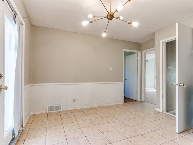 empty room featuring a healthy amount of sunlight, light tile patterned floors, and a chandelier