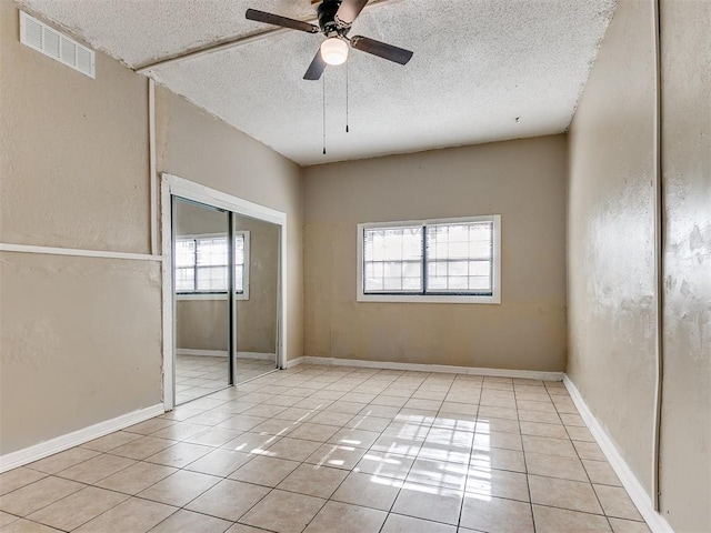 unfurnished bedroom with multiple windows, ceiling fan, light tile patterned floors, and a textured ceiling