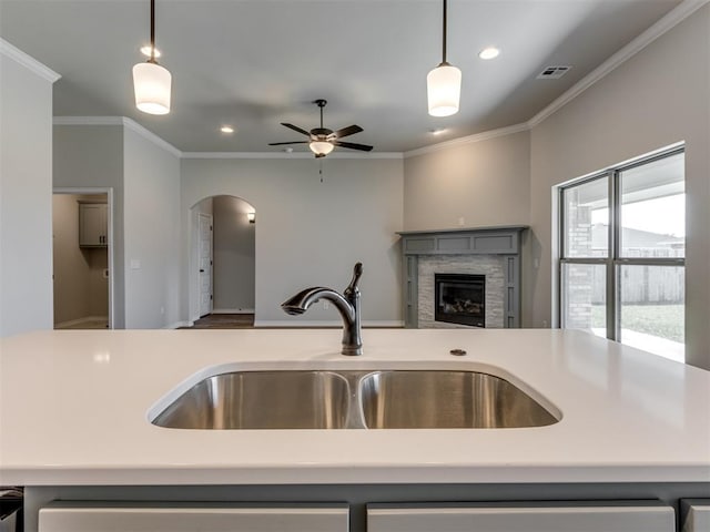 kitchen featuring pendant lighting, a stone fireplace, ornamental molding, and sink