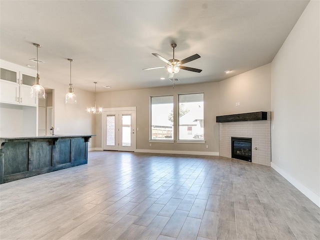 unfurnished living room featuring sink, light hardwood / wood-style flooring, ceiling fan with notable chandelier, and a brick fireplace