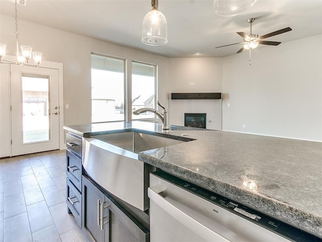 kitchen featuring pendant lighting, stainless steel dishwasher, a wealth of natural light, and a brick fireplace