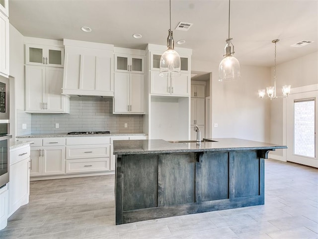 kitchen featuring light stone counters, sink, white cabinetry, hanging light fixtures, and an island with sink