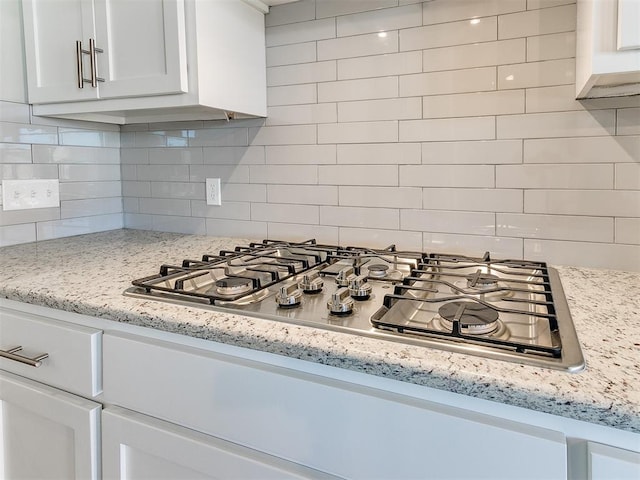 kitchen with white cabinets, stainless steel gas stovetop, light stone countertops, and tasteful backsplash