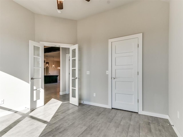 empty room with ceiling fan with notable chandelier, french doors, and light wood-type flooring