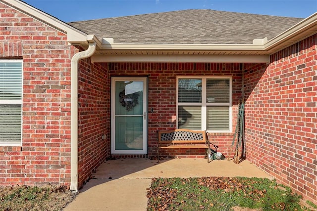 property entrance with a shingled roof and brick siding