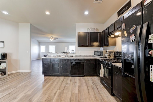 kitchen with light wood finished floors, open floor plan, a peninsula, under cabinet range hood, and black appliances