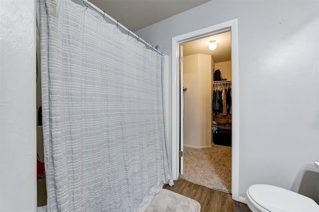 bathroom with a shower with shower curtain, a spacious closet, toilet, and wood finished floors