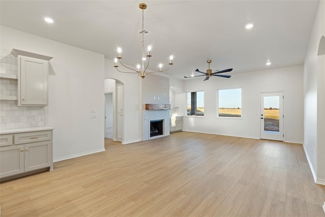 unfurnished living room featuring a fireplace, light hardwood / wood-style flooring, and ceiling fan with notable chandelier