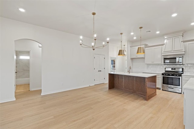 kitchen featuring a kitchen island with sink, pendant lighting, light wood-type flooring, and appliances with stainless steel finishes