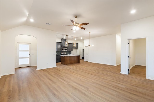 unfurnished living room with ceiling fan with notable chandelier, light wood-type flooring, and lofted ceiling