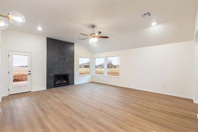 unfurnished living room with a tile fireplace, light hardwood / wood-style flooring, vaulted ceiling, and a healthy amount of sunlight