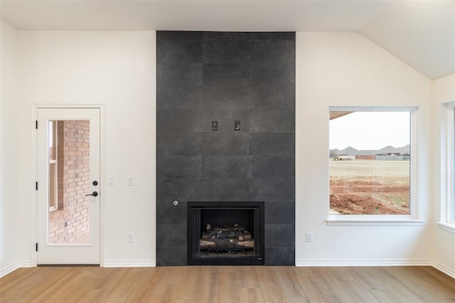 unfurnished living room with a tile fireplace, light hardwood / wood-style floors, and lofted ceiling