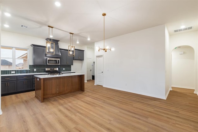 kitchen with hanging light fixtures, stainless steel appliances, backsplash, light hardwood / wood-style floors, and a kitchen island