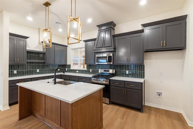 kitchen featuring appliances with stainless steel finishes, light wood-type flooring, a kitchen island with sink, sink, and hanging light fixtures