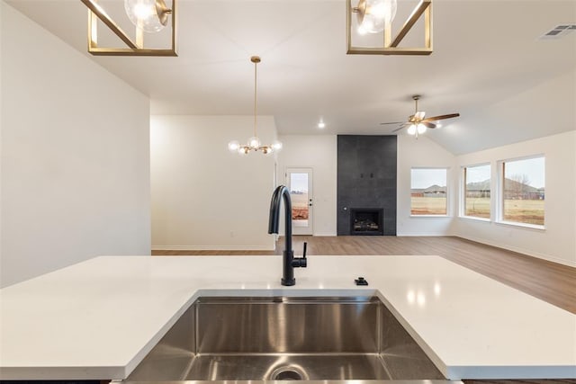 kitchen featuring ceiling fan with notable chandelier, sink, hanging light fixtures, light hardwood / wood-style flooring, and a fireplace