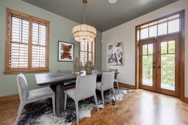 dining space featuring french doors, an inviting chandelier, a healthy amount of sunlight, and light hardwood / wood-style flooring