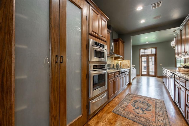 kitchen with light stone countertops, french doors, backsplash, stainless steel gas stovetop, and light wood-type flooring